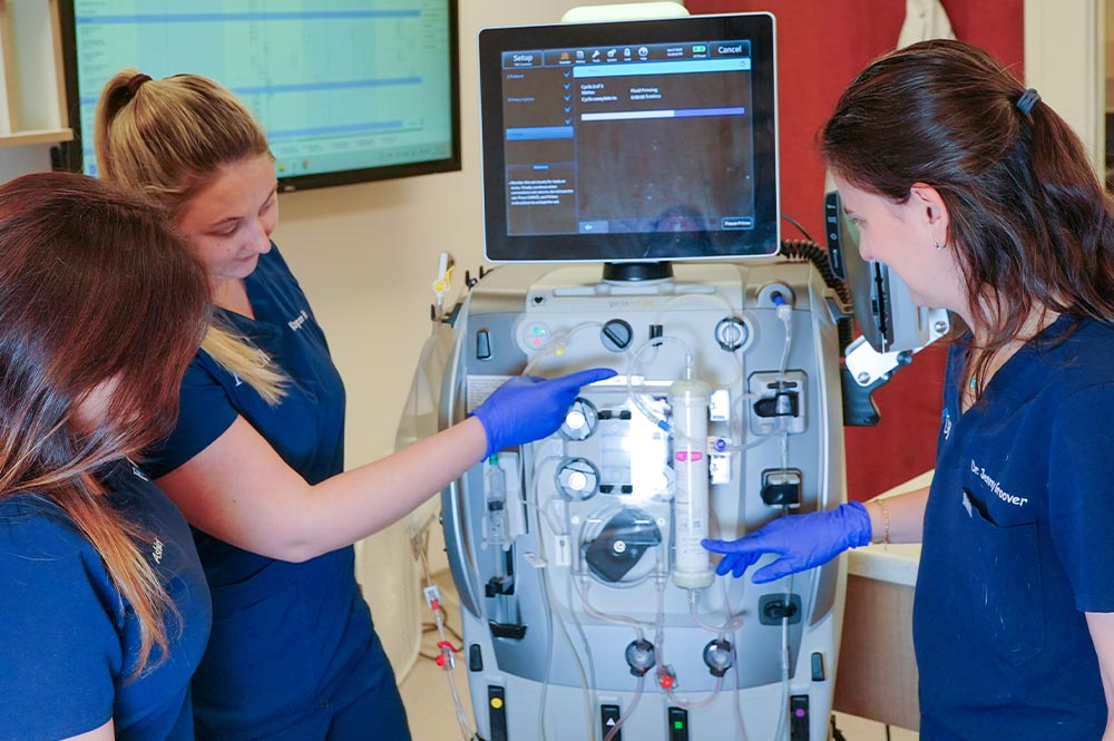 three female staff members pointing and talking about machine