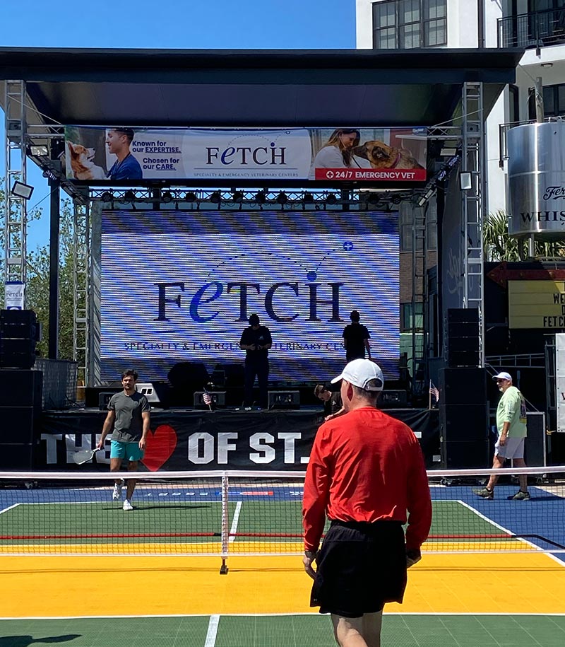 Fetch Vets logo on large digital display behind pickleball court