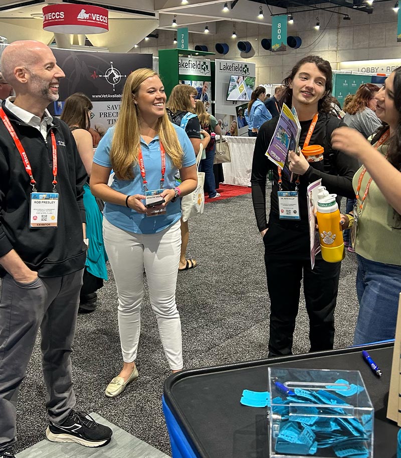 two staff members talking to attendees at IVECCS 2025