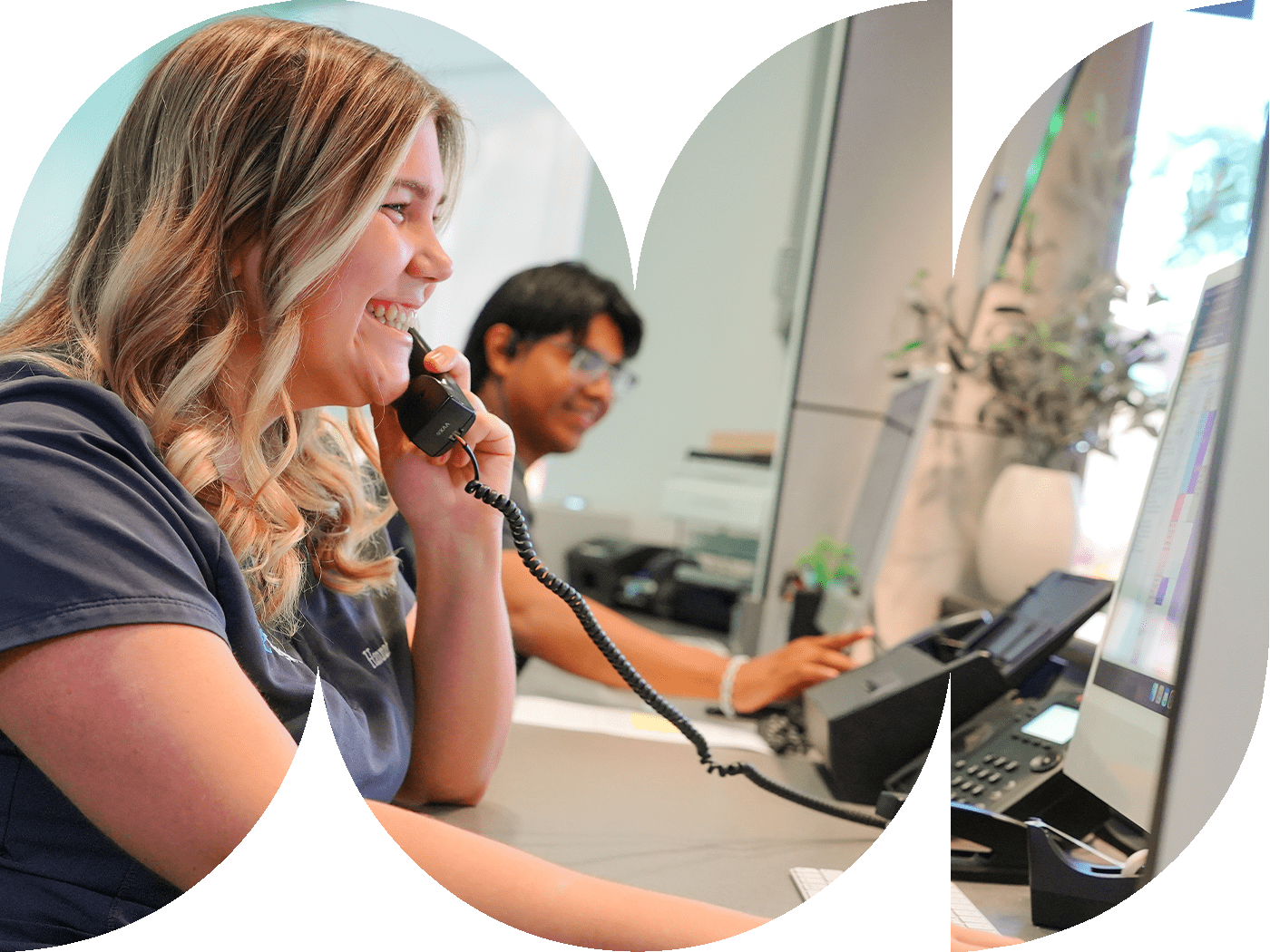 female front desk receptionist smiling while talking on phone and looking at computer