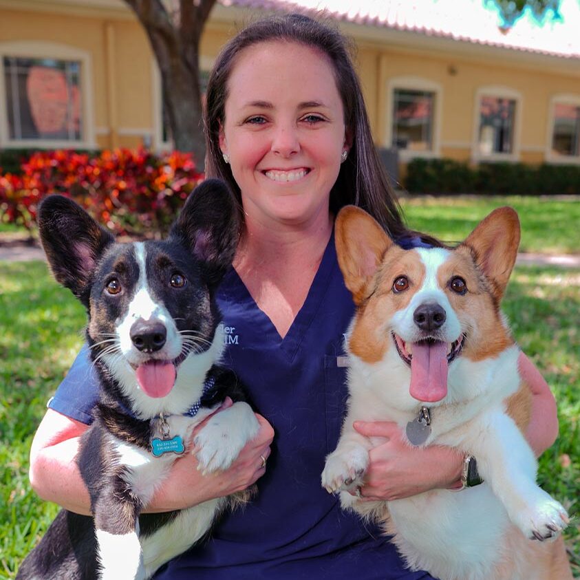 female staff member smiling and posing outdoors with two corgis