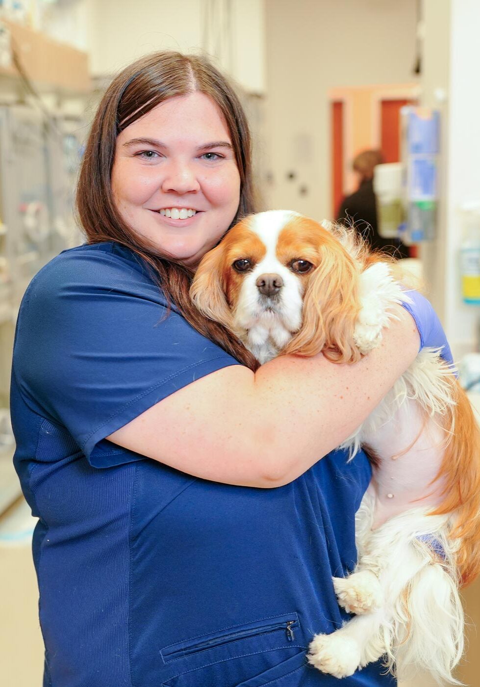 female staff member smiling while holding small cavalier king charles dog